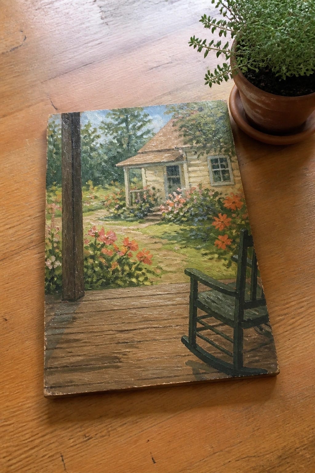 Rustic painting of green rocking chair on porch overlooking flower garden and cottage