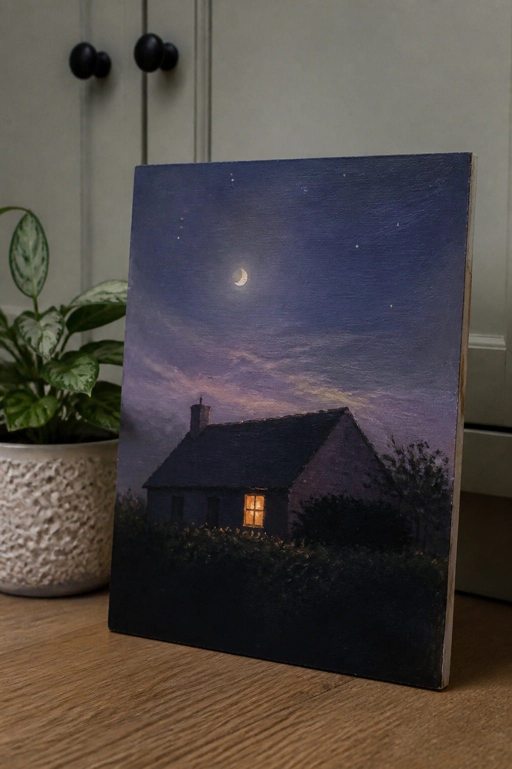 Painting of dark cottage with glowing window under crescent moon and starry purple sky beside plant