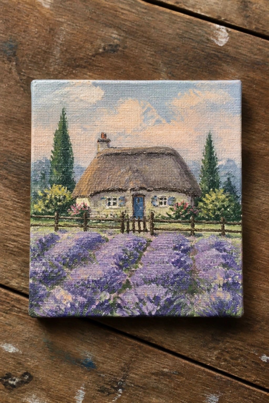 Small square canvas painting of thatched cottage amid purple lavender field on wood