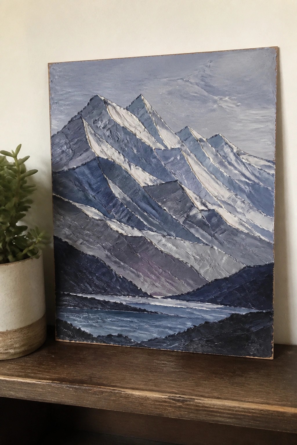 Textured blue-and-white impasto painting of snowy mountains beside a potted plant.