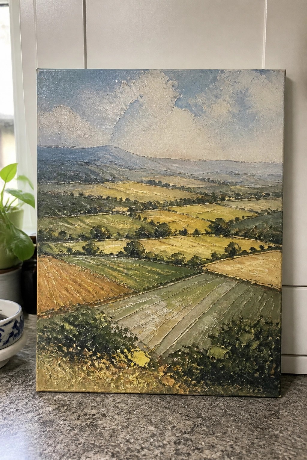 Thickly textured landscape painting of rolling hills, patchwork fields, and cloudy blue sky