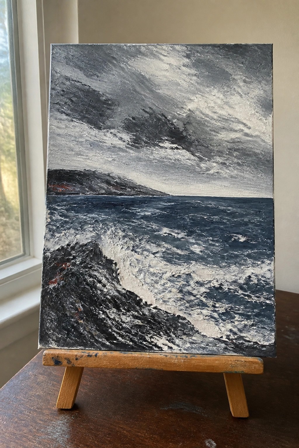 Textured seascape painting of dark crashing waves under stormy gray sky on easel.