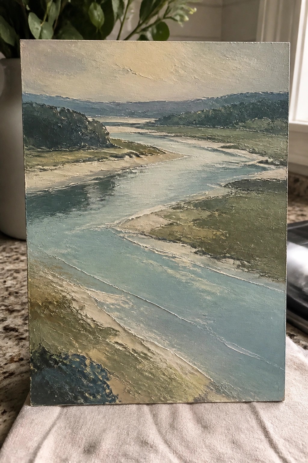 An oil painting of a winding blue river flowing through green and sandy terrain with hills in the background.