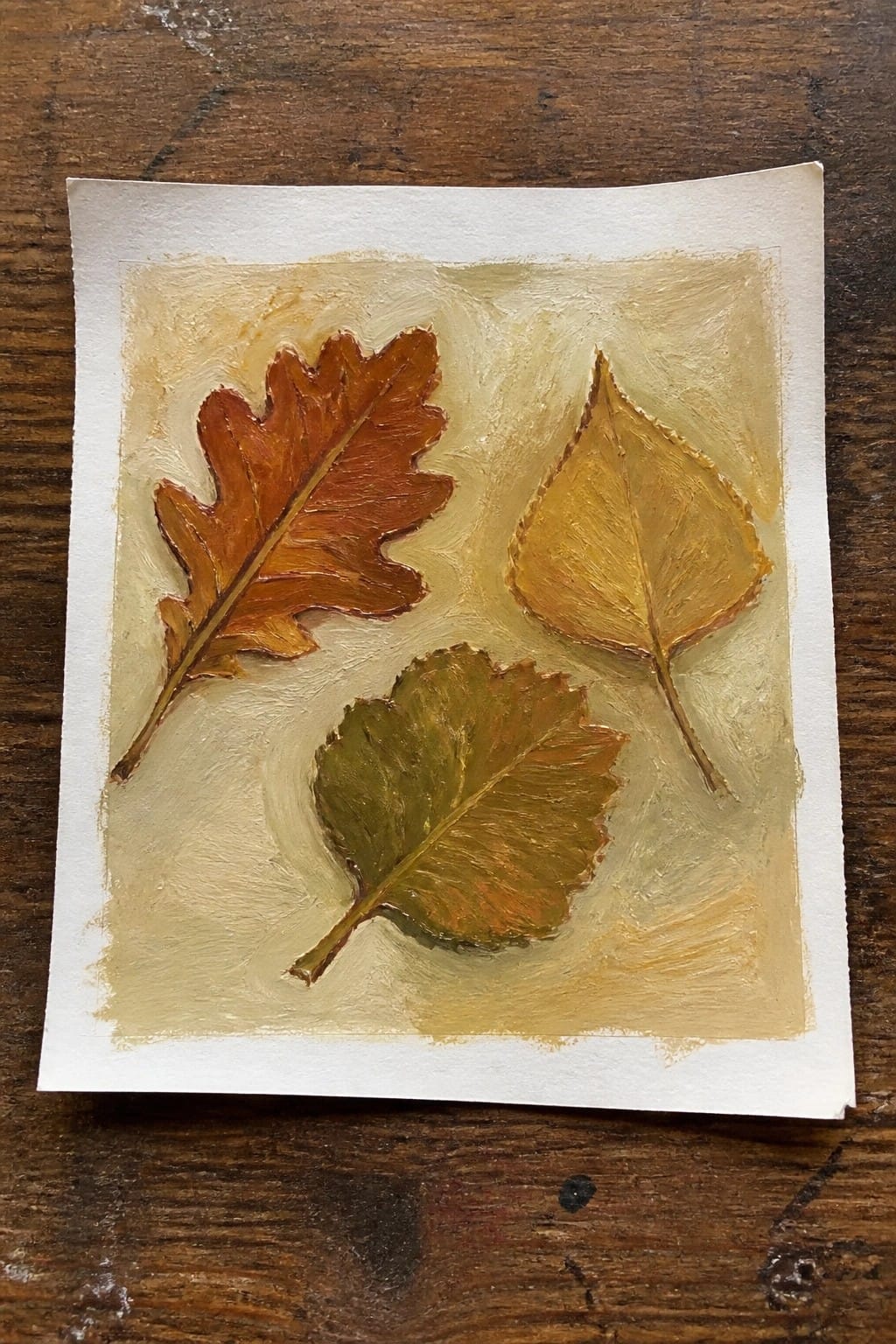 Three autumn leaves painted in orange, yellow, and green on textured paper.