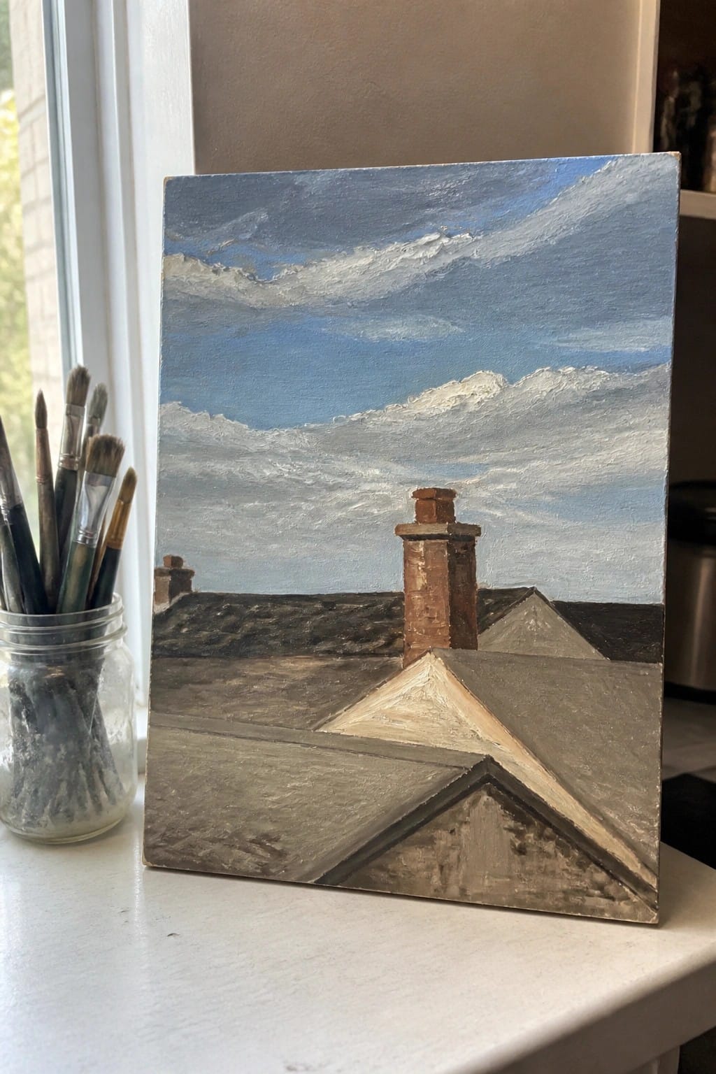 Painting of rooftops and chimneys under cloudy blue sky beside paintbrushes