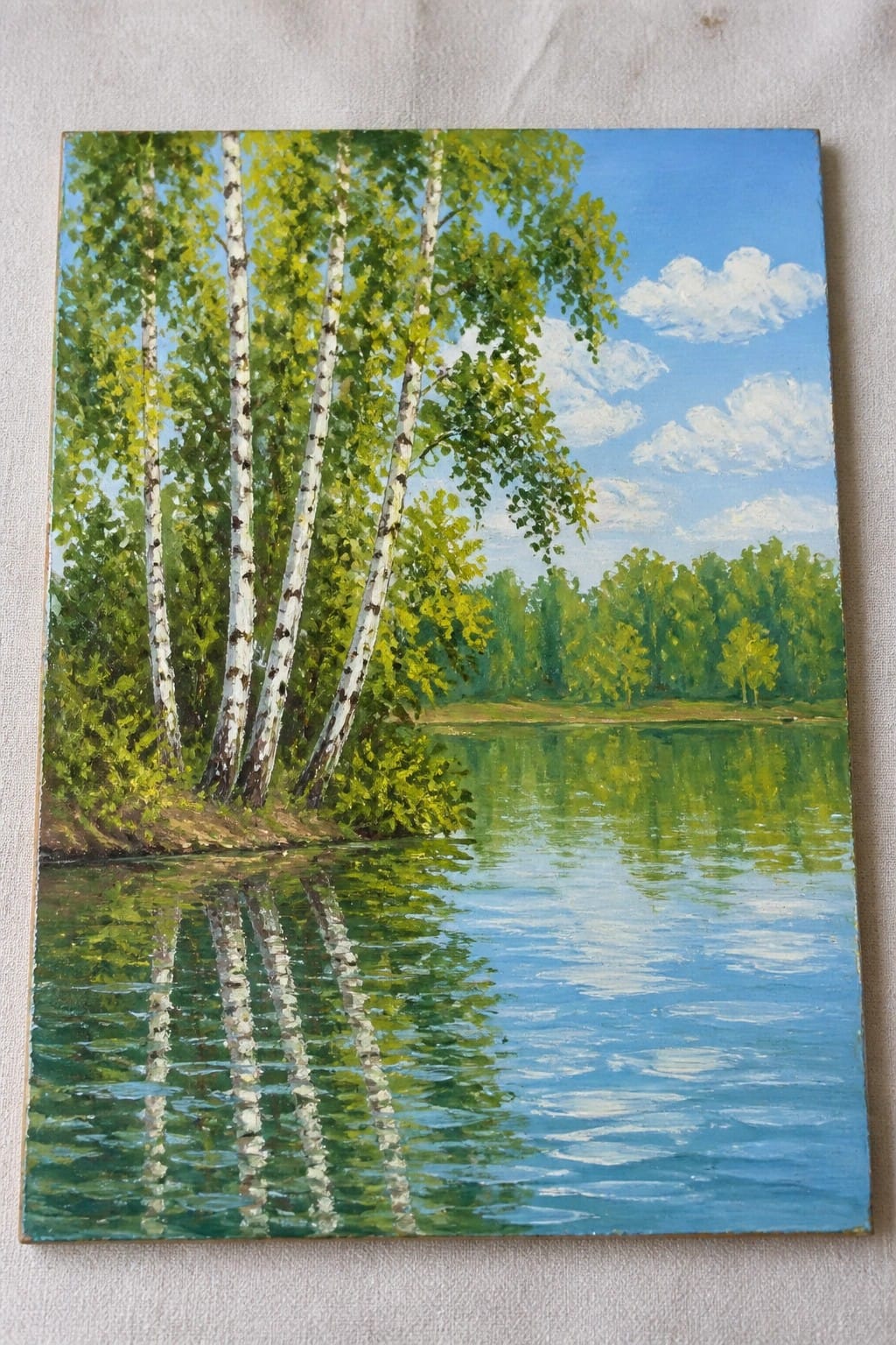 An oil painting of white birch trees along a lake shore with their reflections in the blue water and green forest in the background under a cloudy sky.