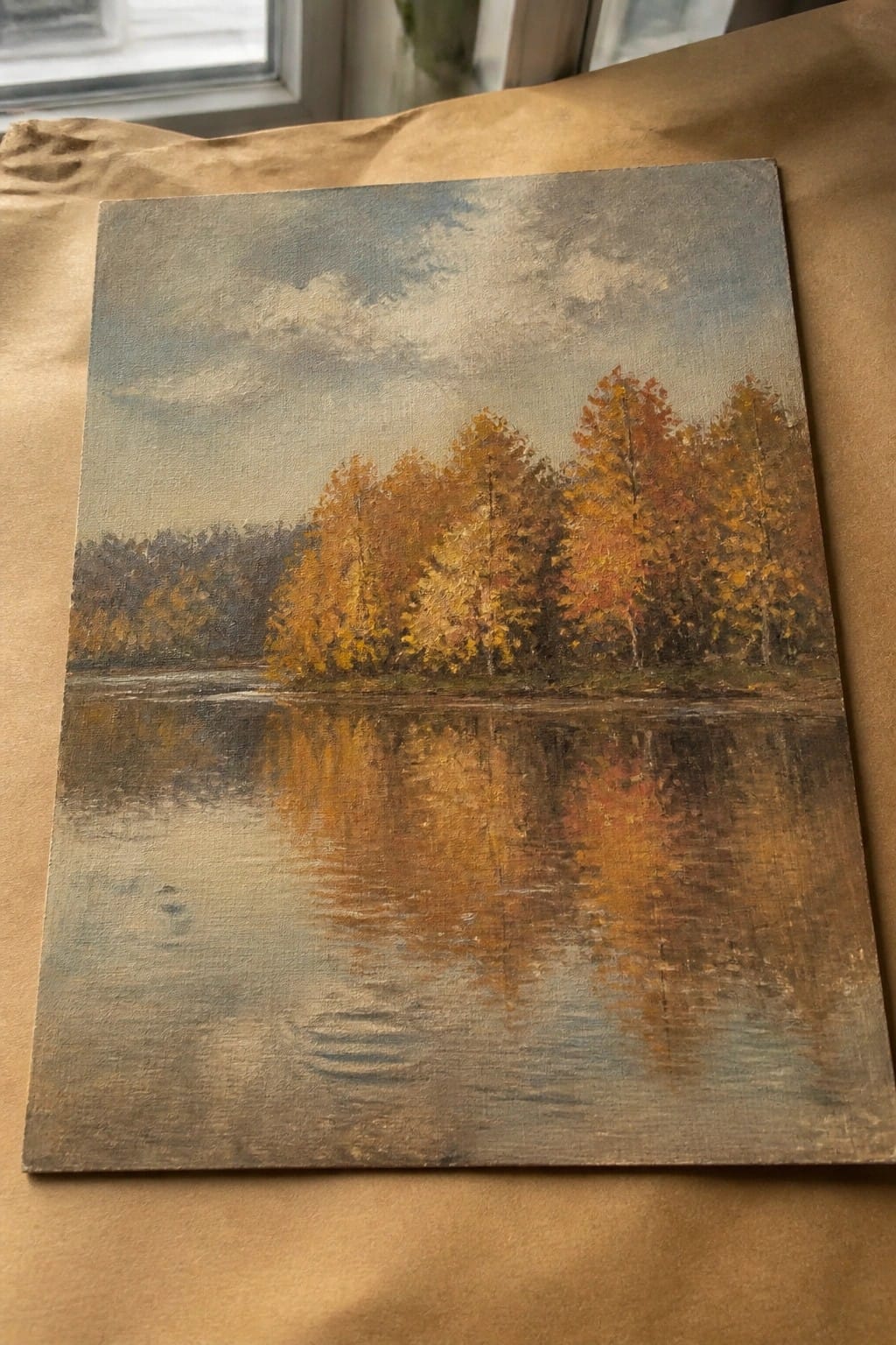 Autumn landscape painting with orange-yellow trees reflected in calm water under cloudy sky.