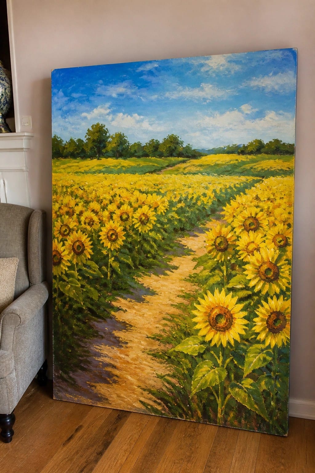 Large painting of yellow sunflowers along winding path under blue sky leaning indoors