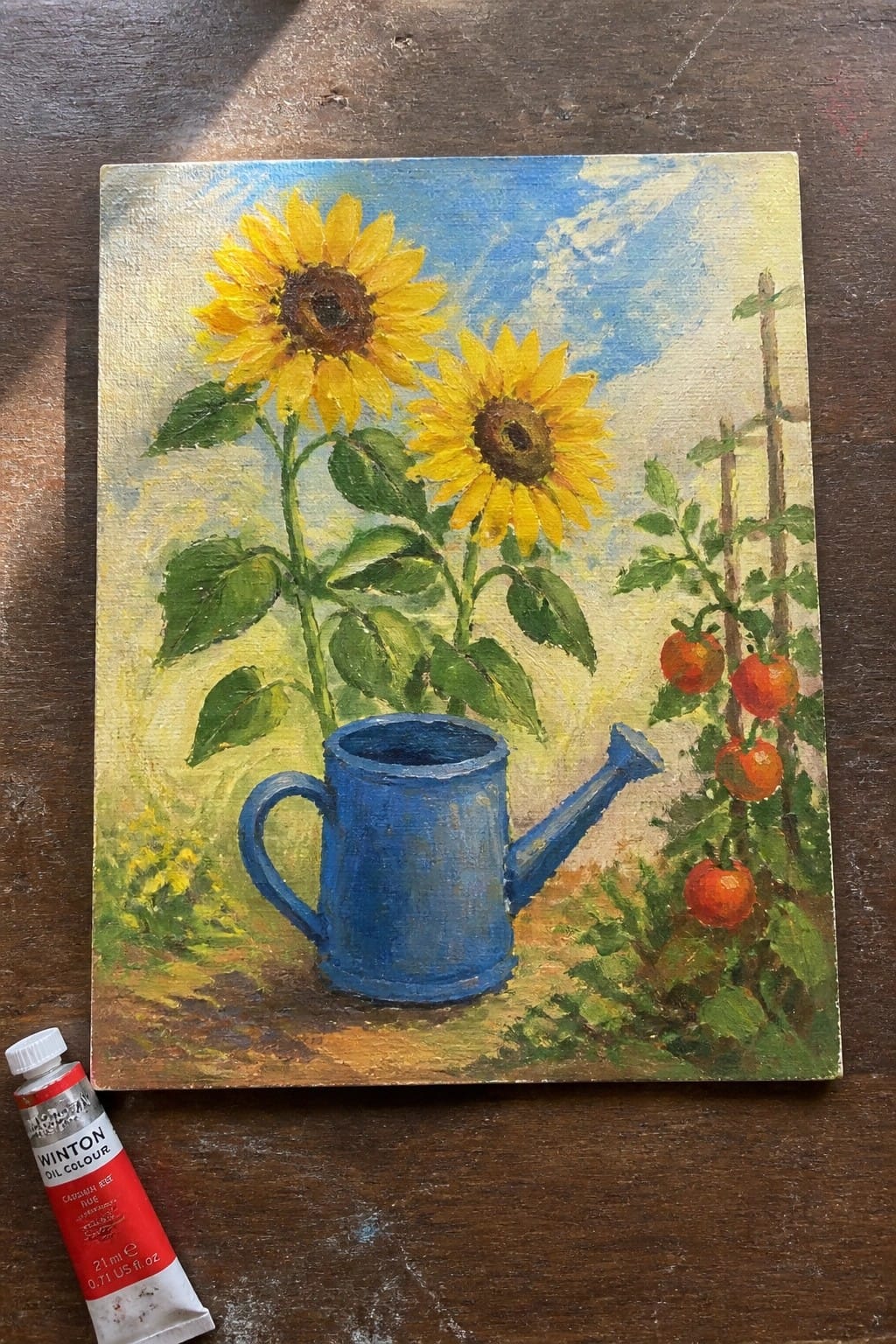 Yellow sunflowers in blue watering can beside tomato vines and red paint tube