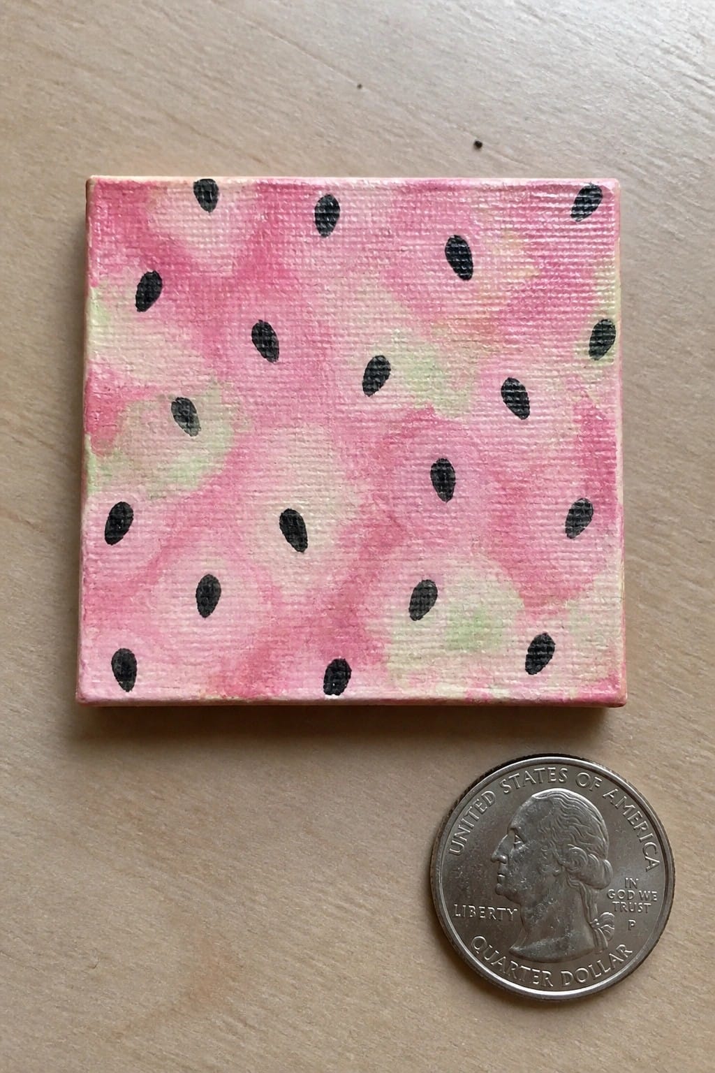 Miniature pink watermelon painting with black seeds beside a quarter coin