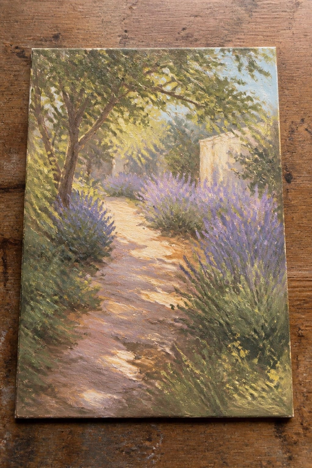 Sunlit dirt path winding through blooming purple lavender bushes and leafy trees.