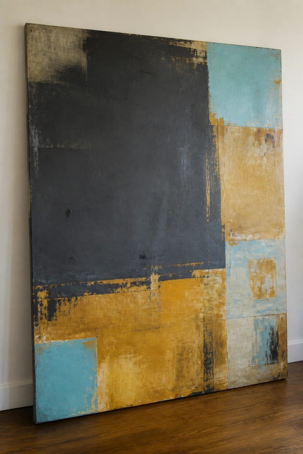 Large abstract painting with black, turquoise, yellow, and beige blocks leaning on wall