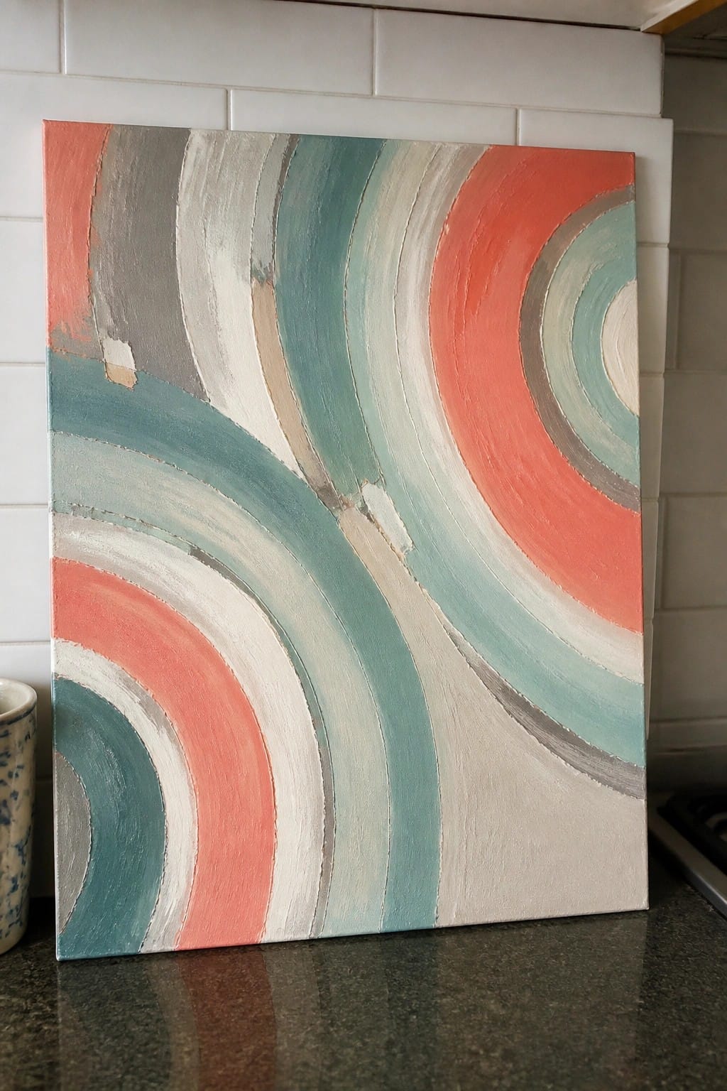 Abstract painting with swirling coral, teal, and gray arcs on kitchen counter