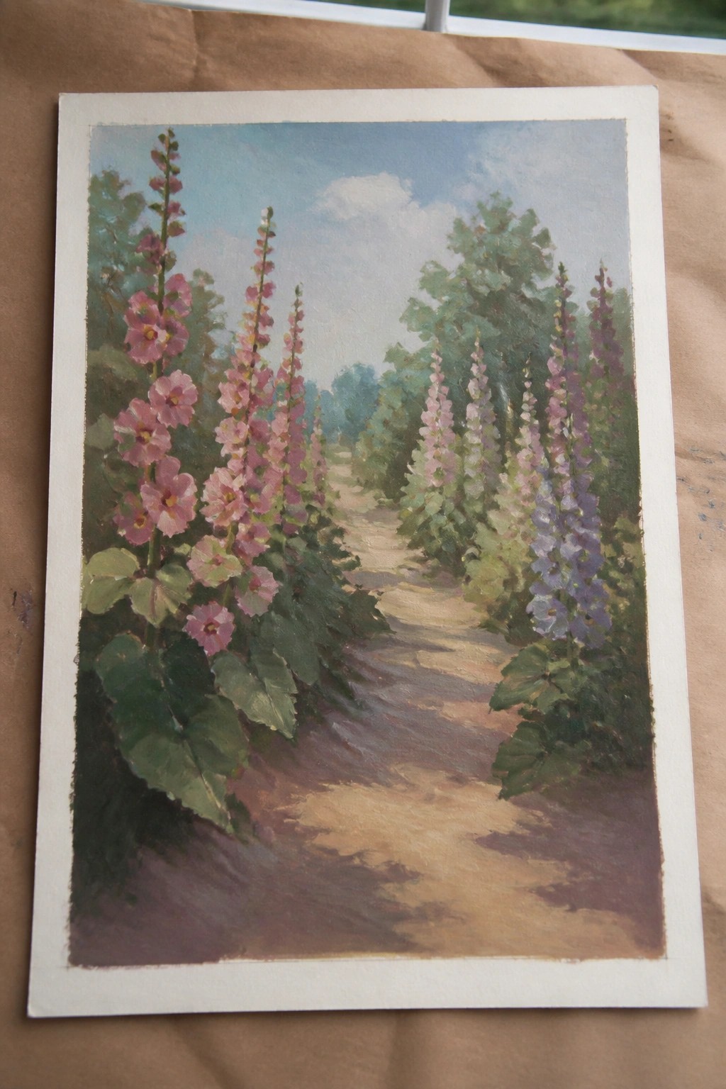 Oil painting of pink and purple hollyhocks lining a sunlit dirt path through trees.