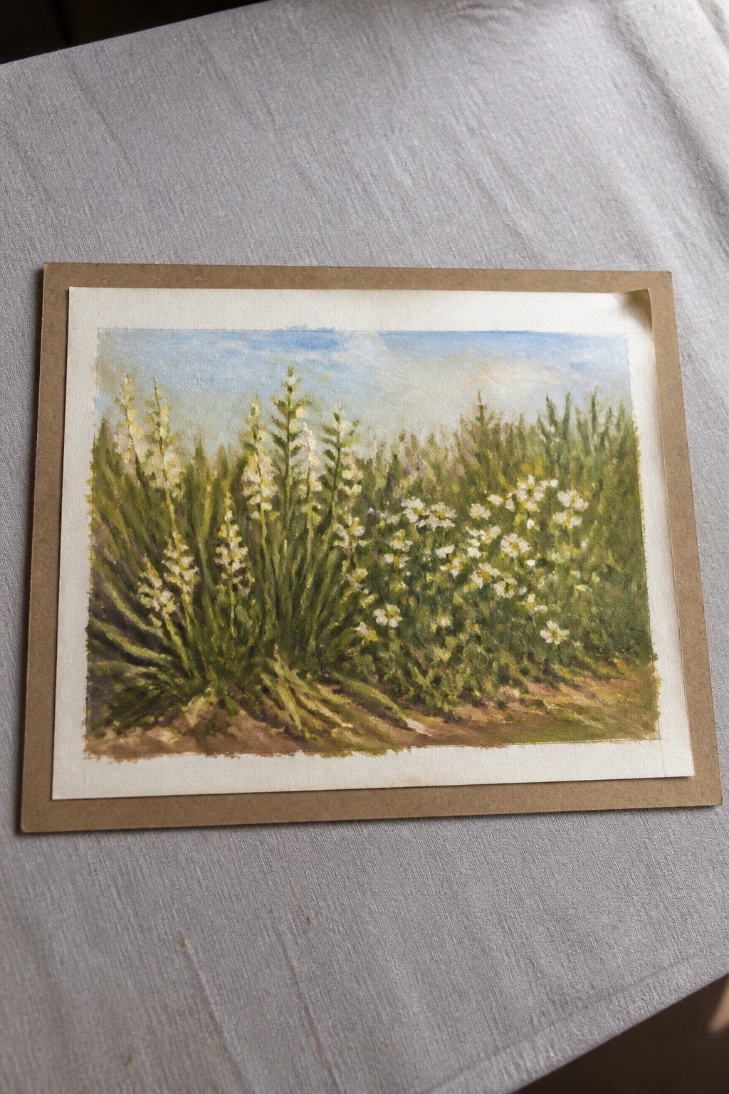 Brown-matted watercolor of white wildflowers blooming in a lush green meadow