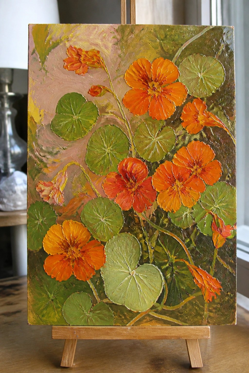 An oil painting of orange nasturtium flowers and green round leaves on a wooden easel.