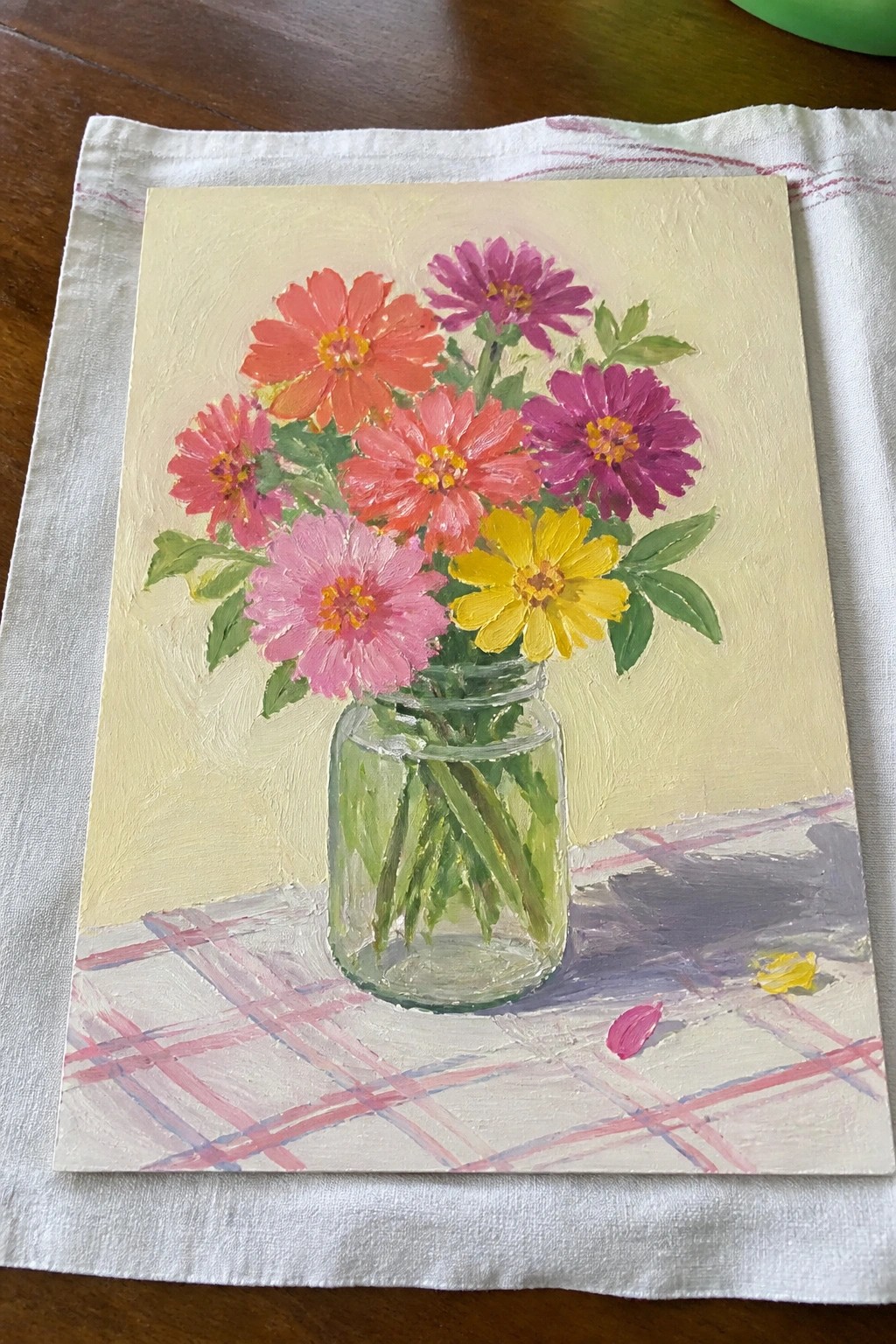 Vibrant pink red purple yellow zinnias in glass jar on checkered cloth