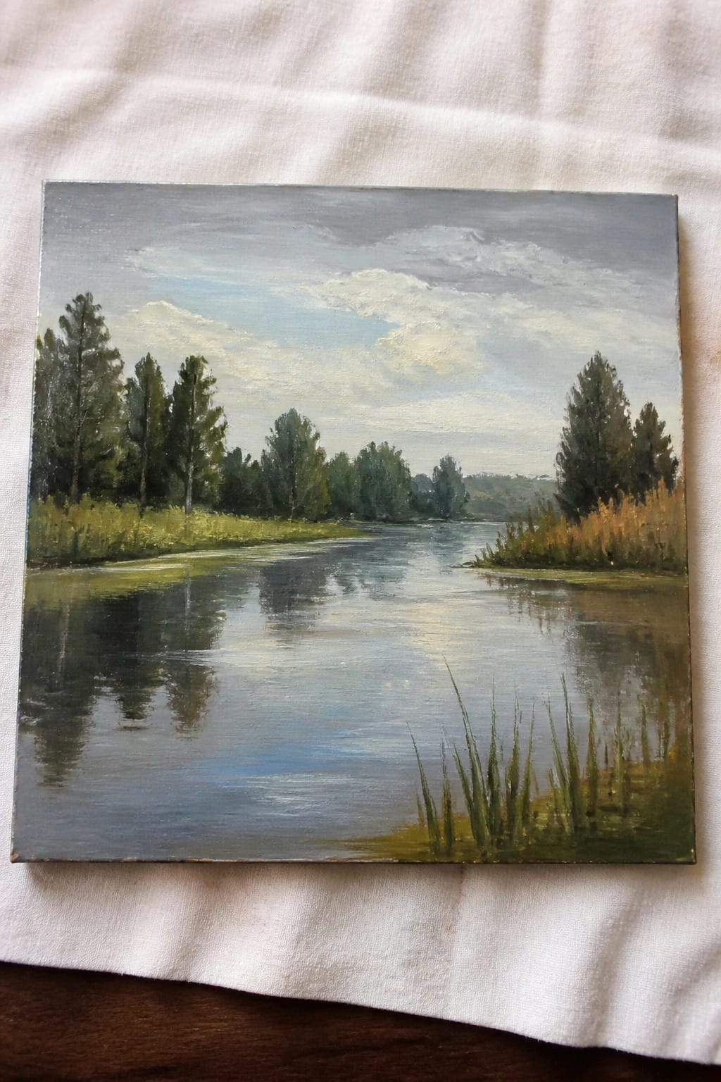 Oil painting of calm river with tree reflections under cloudy sky on white cloth