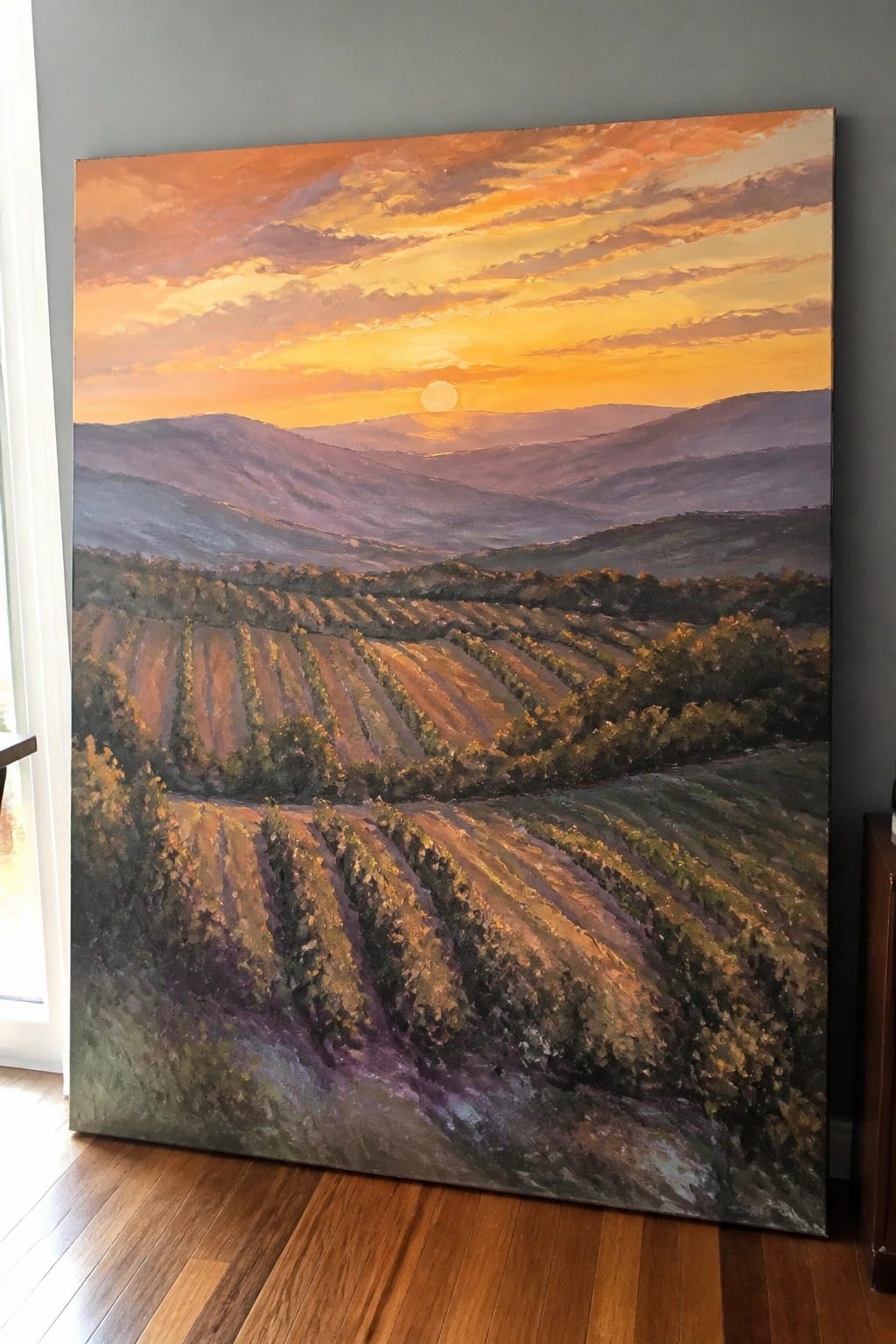 Large painting of vibrant sunset over rolling vineyard hills leaning on gray wall
