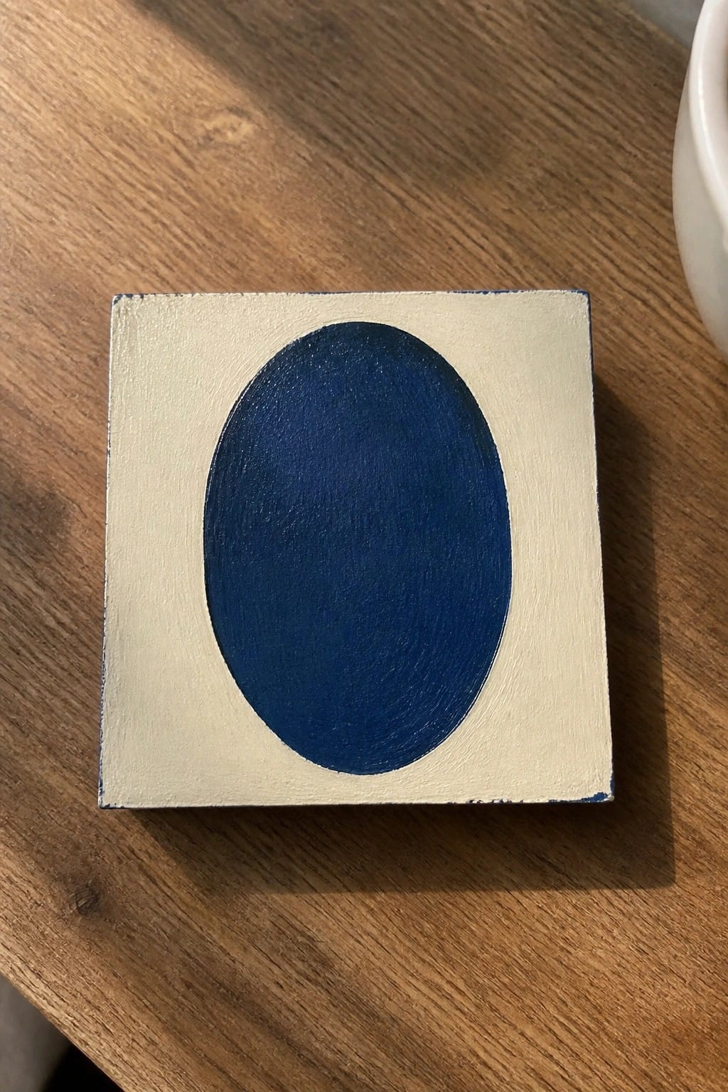 Square canvas with large blue oval on off-white background on wood table.