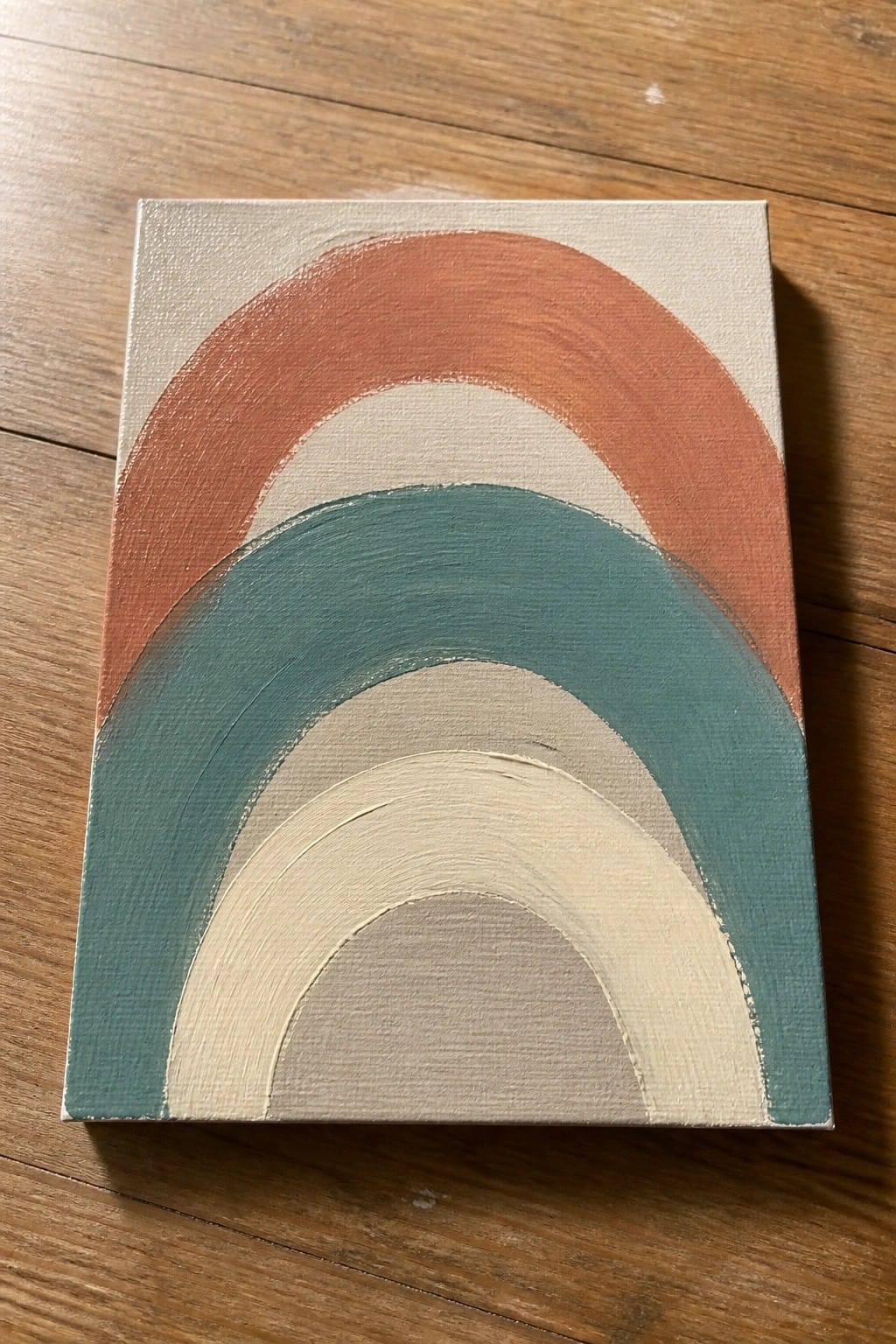 Boho rainbow painting on canvas with terracotta, teal, and beige arches on wood.