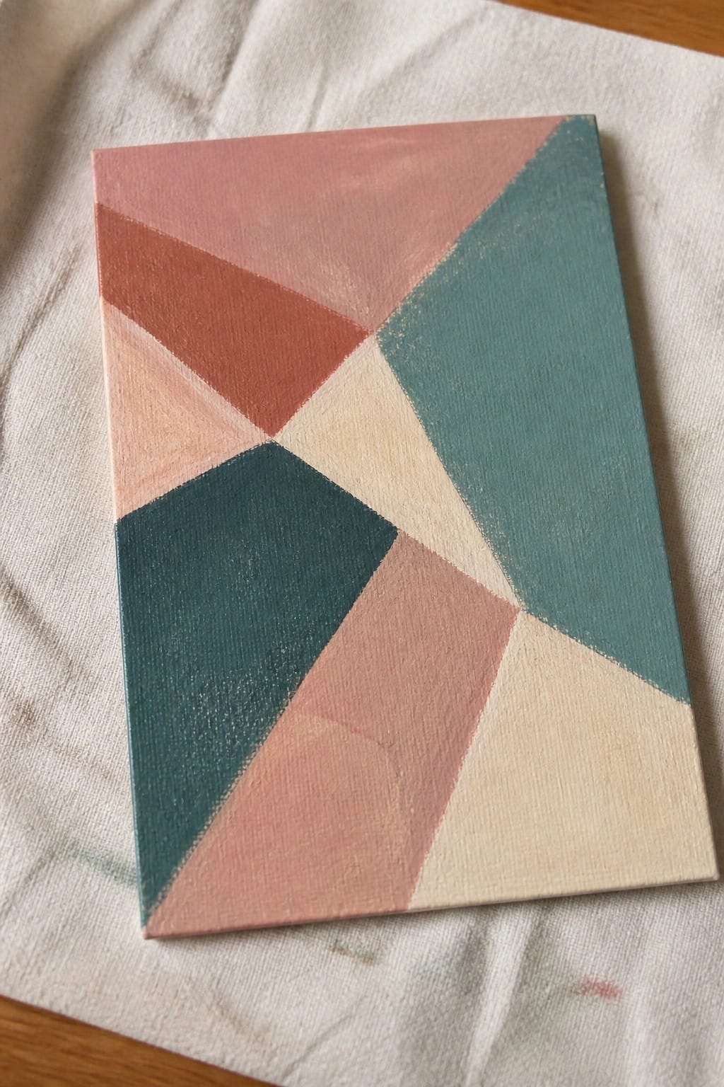 Geometric abstract canvas painting with pink, teal, coral, and beige triangles on white fabric.