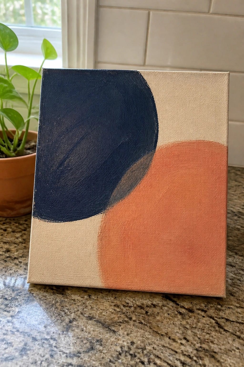 Abstract painting with navy blue and coral orange shapes on kitchen countertop near plant