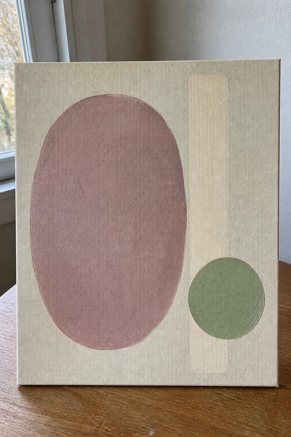 Abstract canvas with large pink oval, small green circle, and vertical beige stripe on wood.