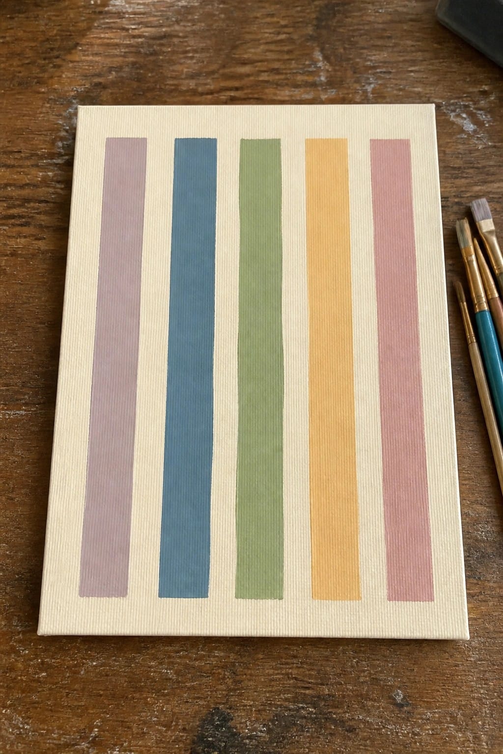 Small canvas with five vertical pastel stripes in purple blue green yellow and pink beside brushes