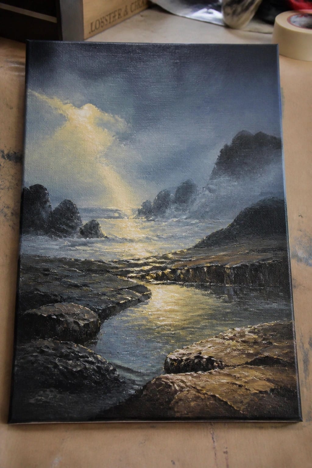 Dramatic oil painting of rocky coastline with golden sunlight piercing stormy clouds.