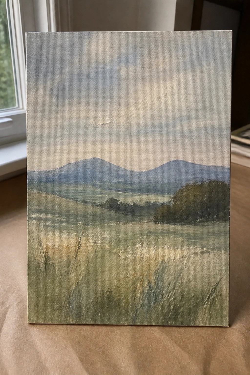 Rectangular canvas painting of misty green hills and distant blue mountains under soft sky.