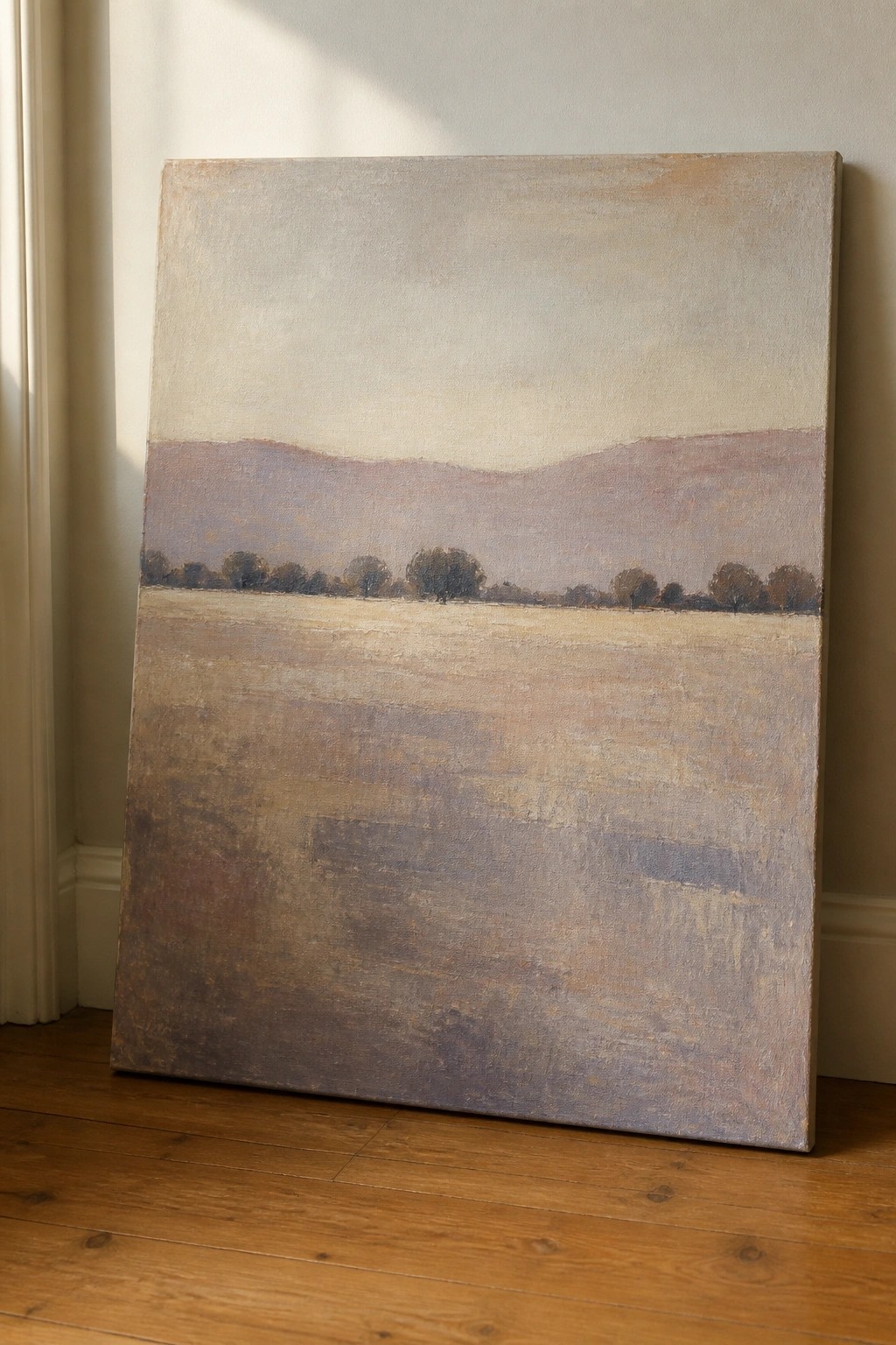 Large muted landscape painting of fields and hills leaning on wooden floor