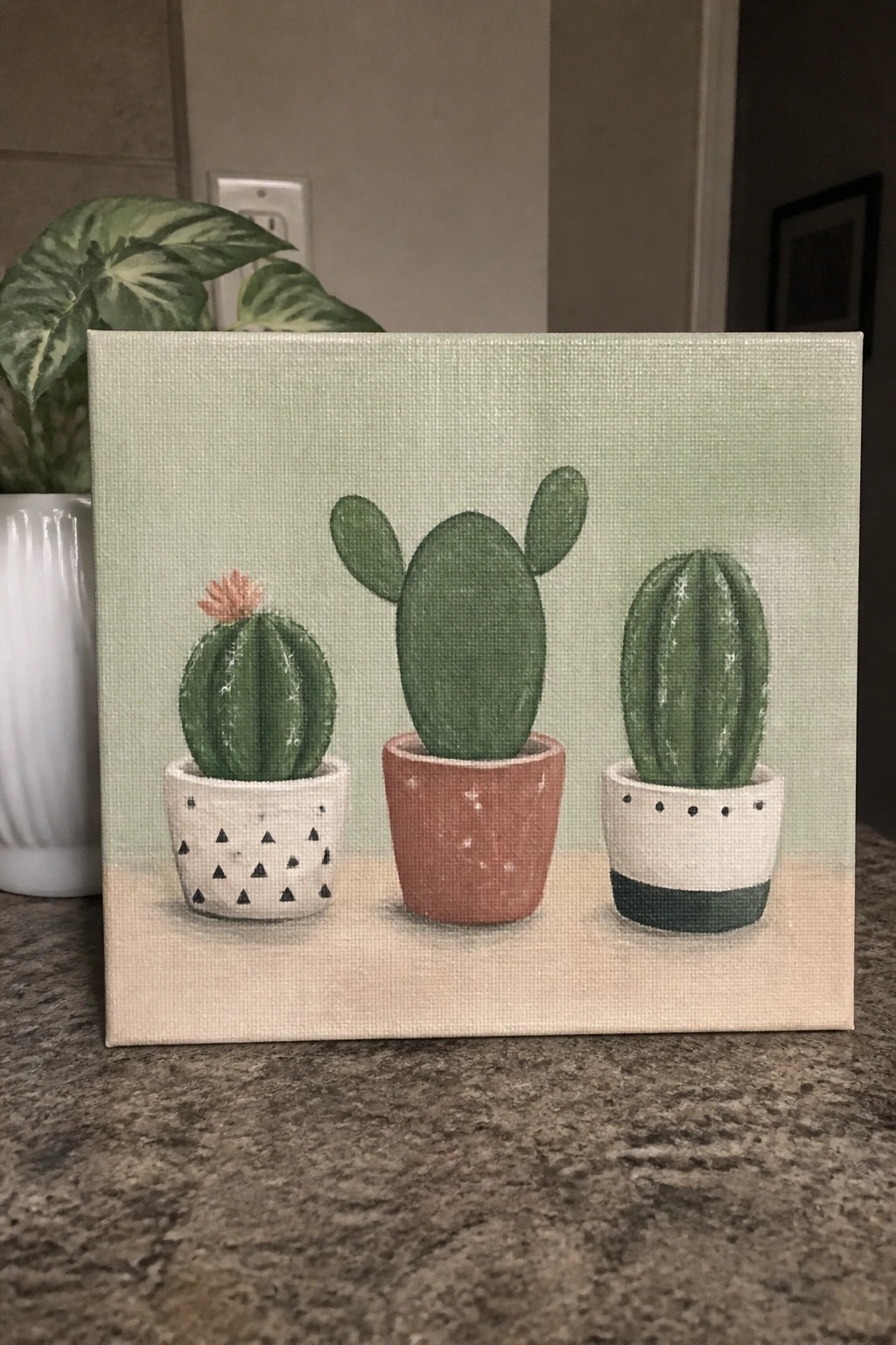Three painted cacti in patterned pots on light green canvas with beige base.
