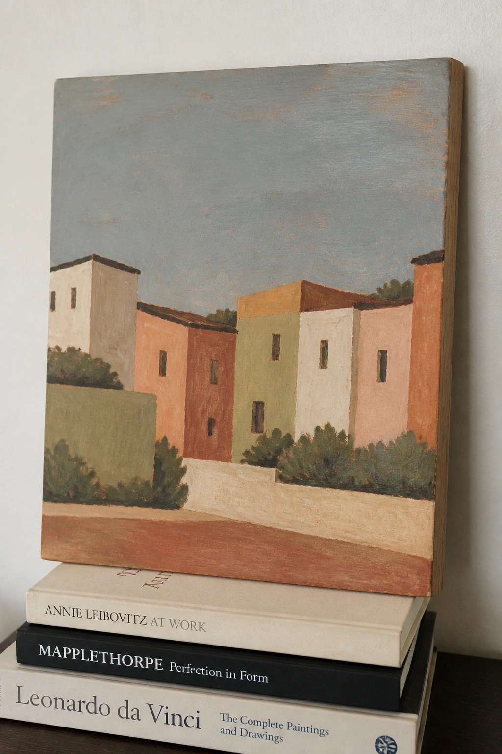Pastel painting of colorful buildings atop art books by Leibovitz and Mapplethorpe.