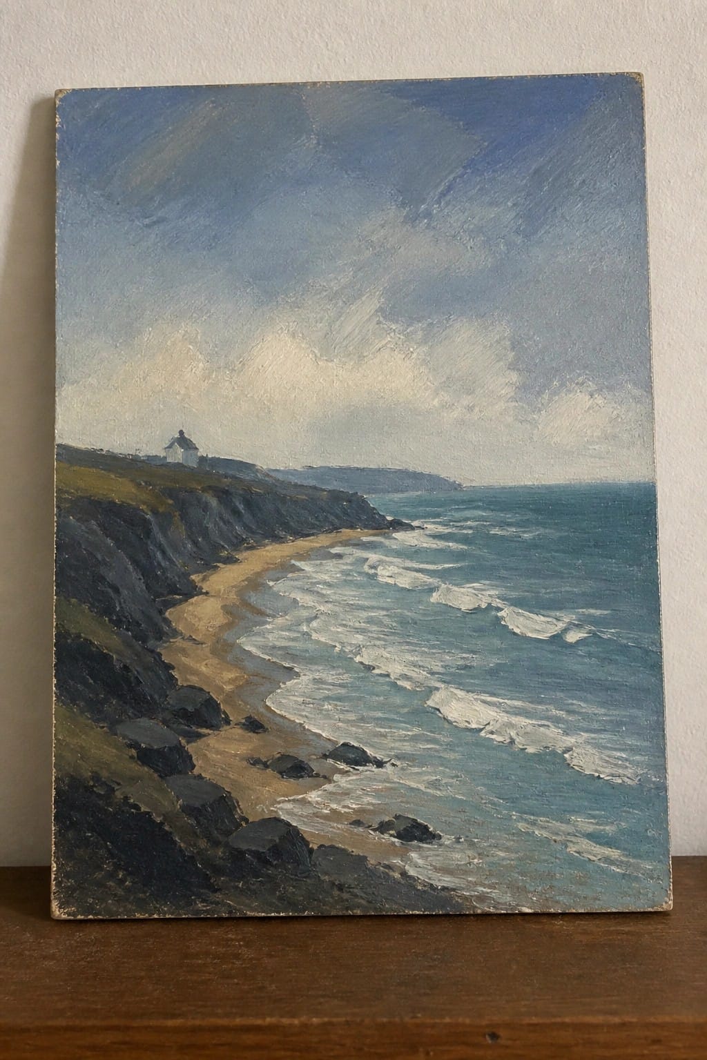 Oil painting of rocky cliffs, sandy beach, and blue sea with white waves.