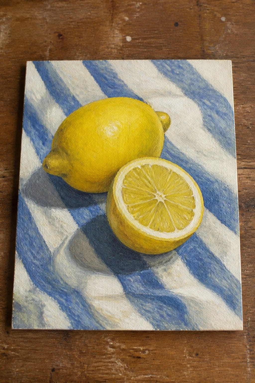 Whole and halved lemon on blue-white striped cloth over wooden surface