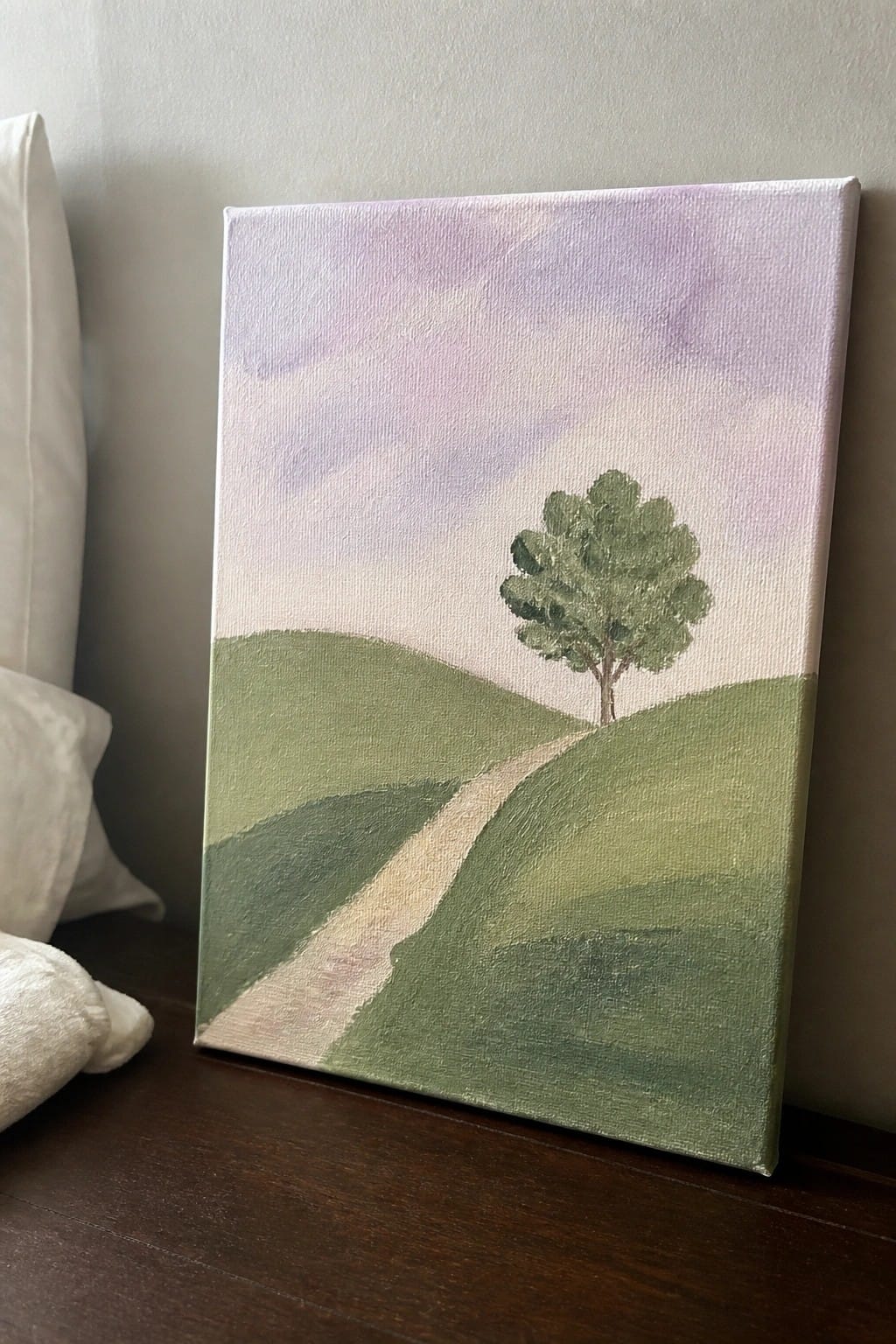 Landscape painting of green hills, winding path, and lone tree under purple sky