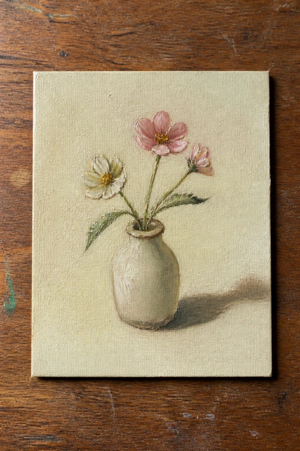 Small white vase with pink and white flowers casting shadow on wood