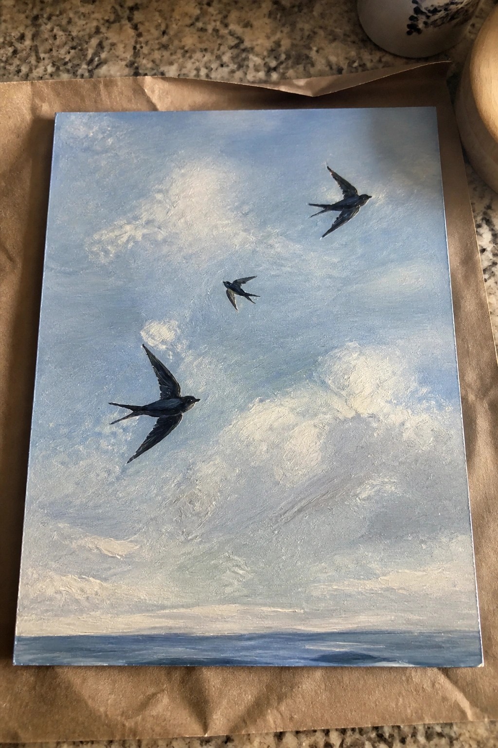 Three black birds soaring in a cloudy blue sky above the sea