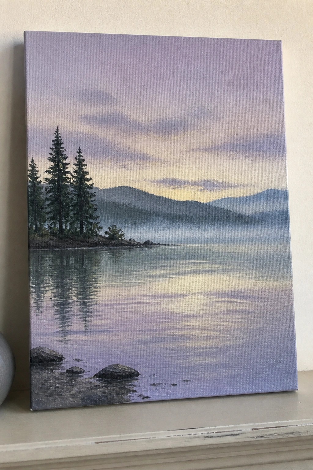 Twilight landscape painting of misty lake with pine trees and mountain reflections.