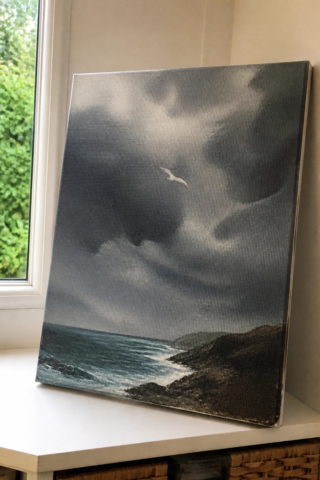 Stormy seascape painting with seagull over rocky coastline on windowsill