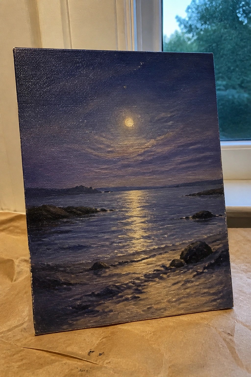 Canvas painting of moonlit ocean with golden reflections on dark rocky shoreline.