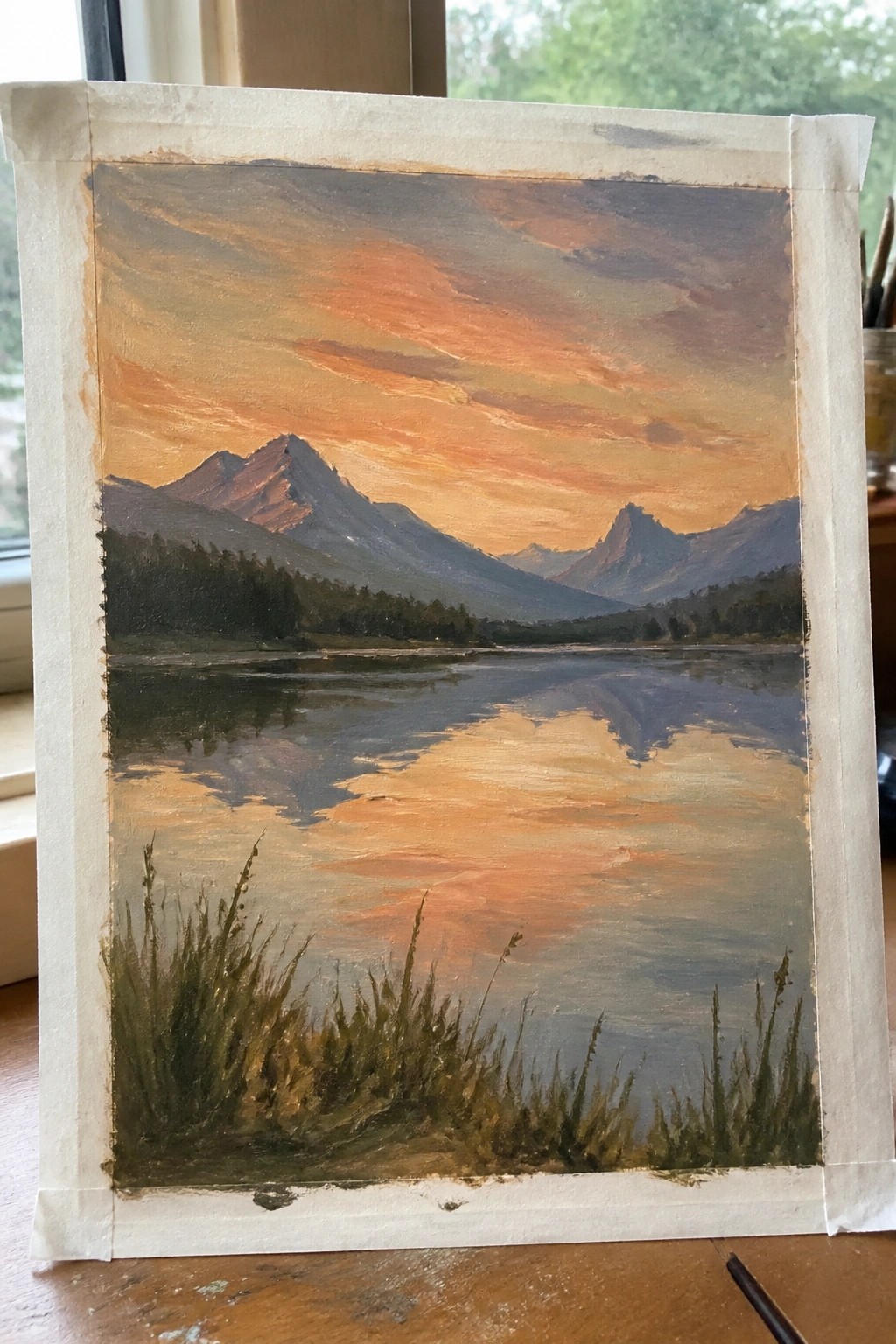 Mountain landscape painting with lake reflection under orange sunset sky and foreground grass