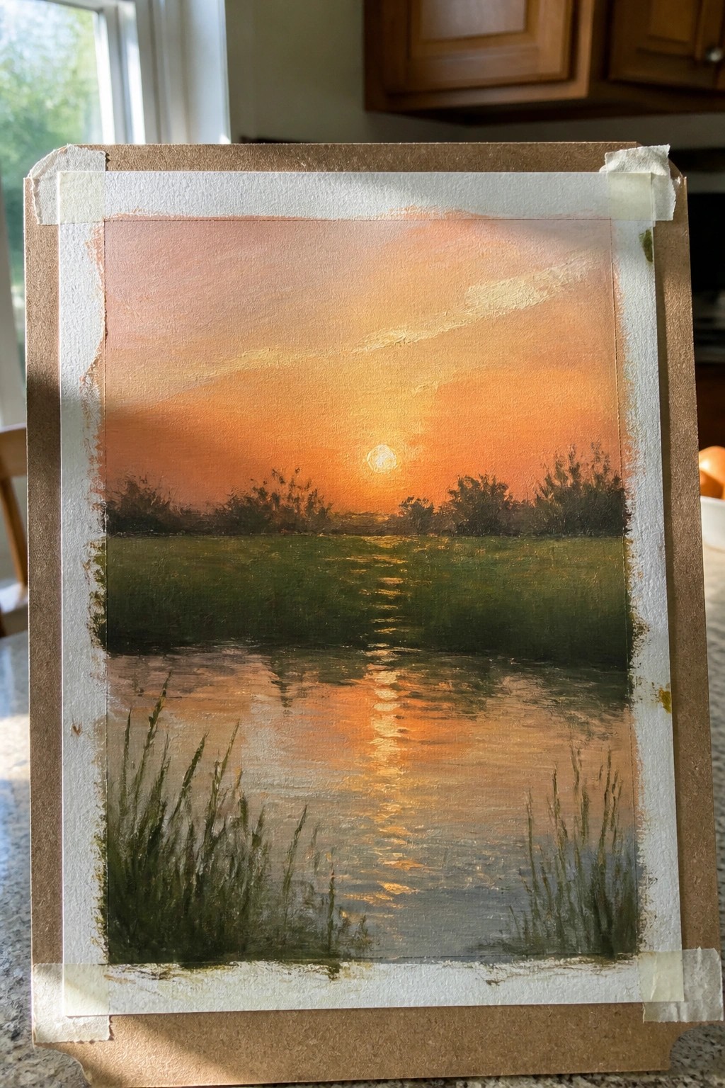 Sunset landscape painting with orange sky, water reflection, and grass, taped to board.