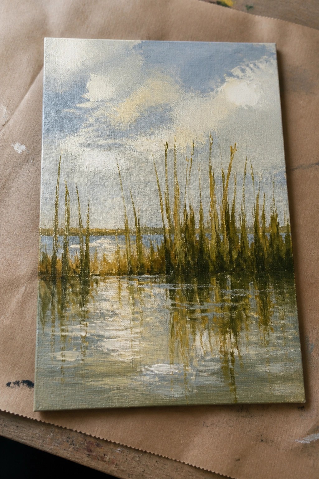 Oil painting of tall green reeds reflected in calm water under cloudy blue sky