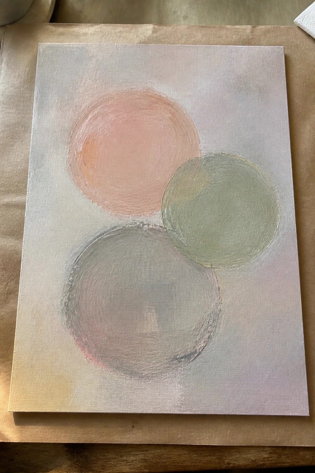 Abstract painting of three overlapping pastel circles in peach, green, and gray on light canvas