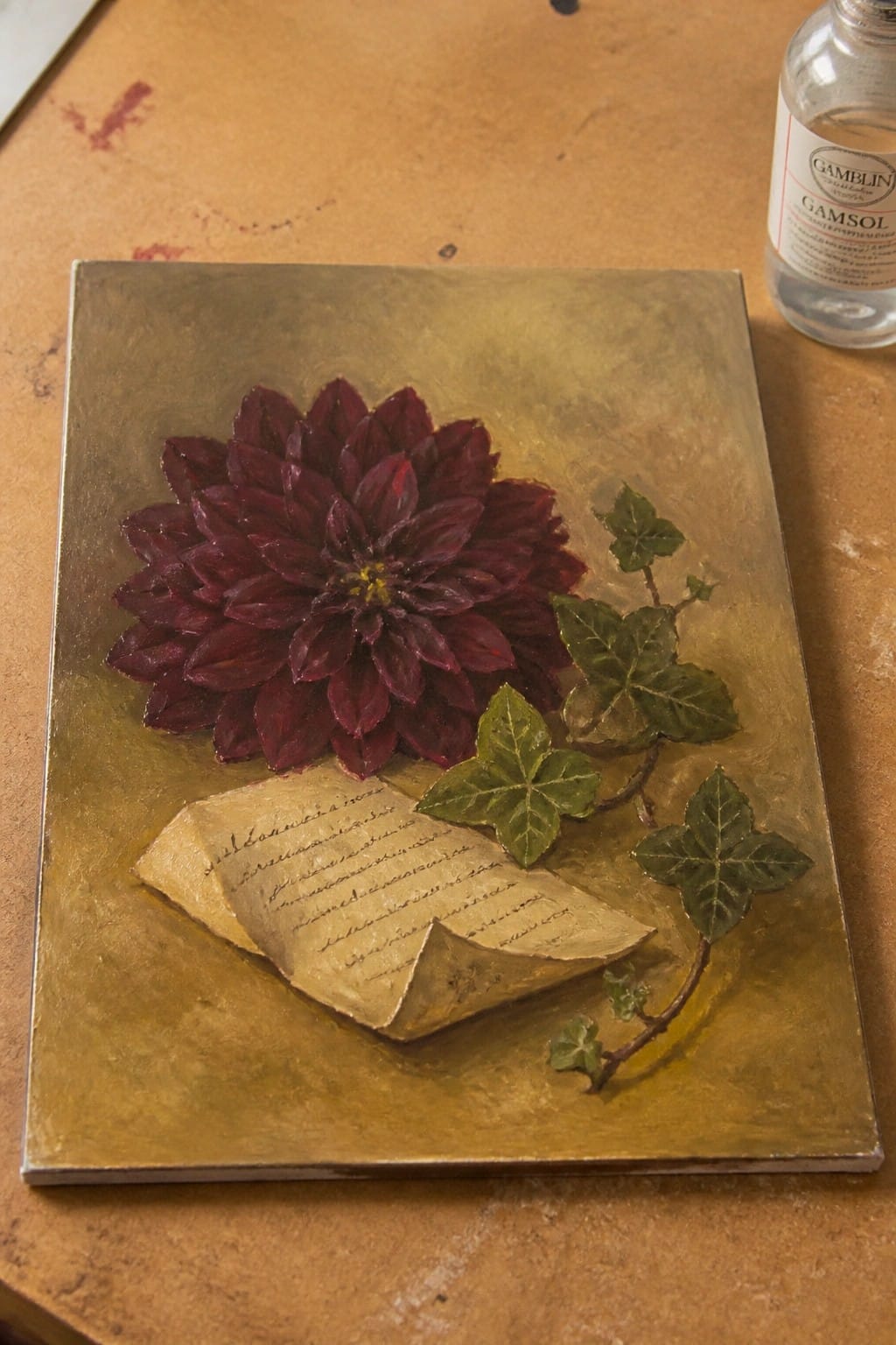 Dark red dahlia, green ivy, and handwritten note on textured gold painting beside Gamsol bottle.