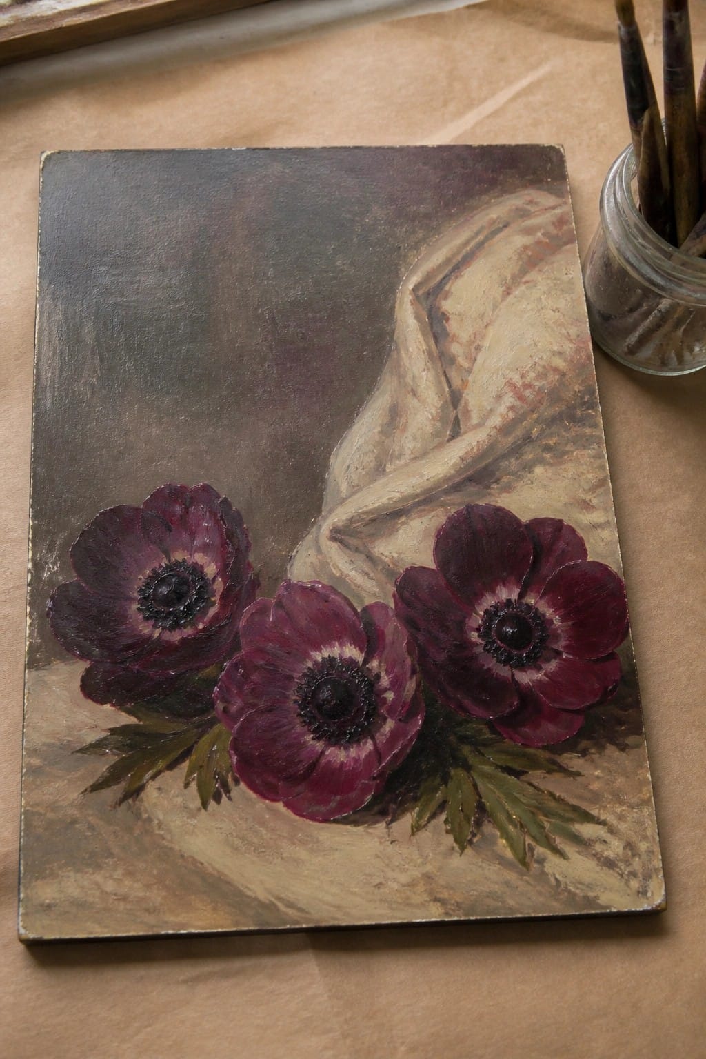 Three dark purple anemones in oil painting beside jar of brushes