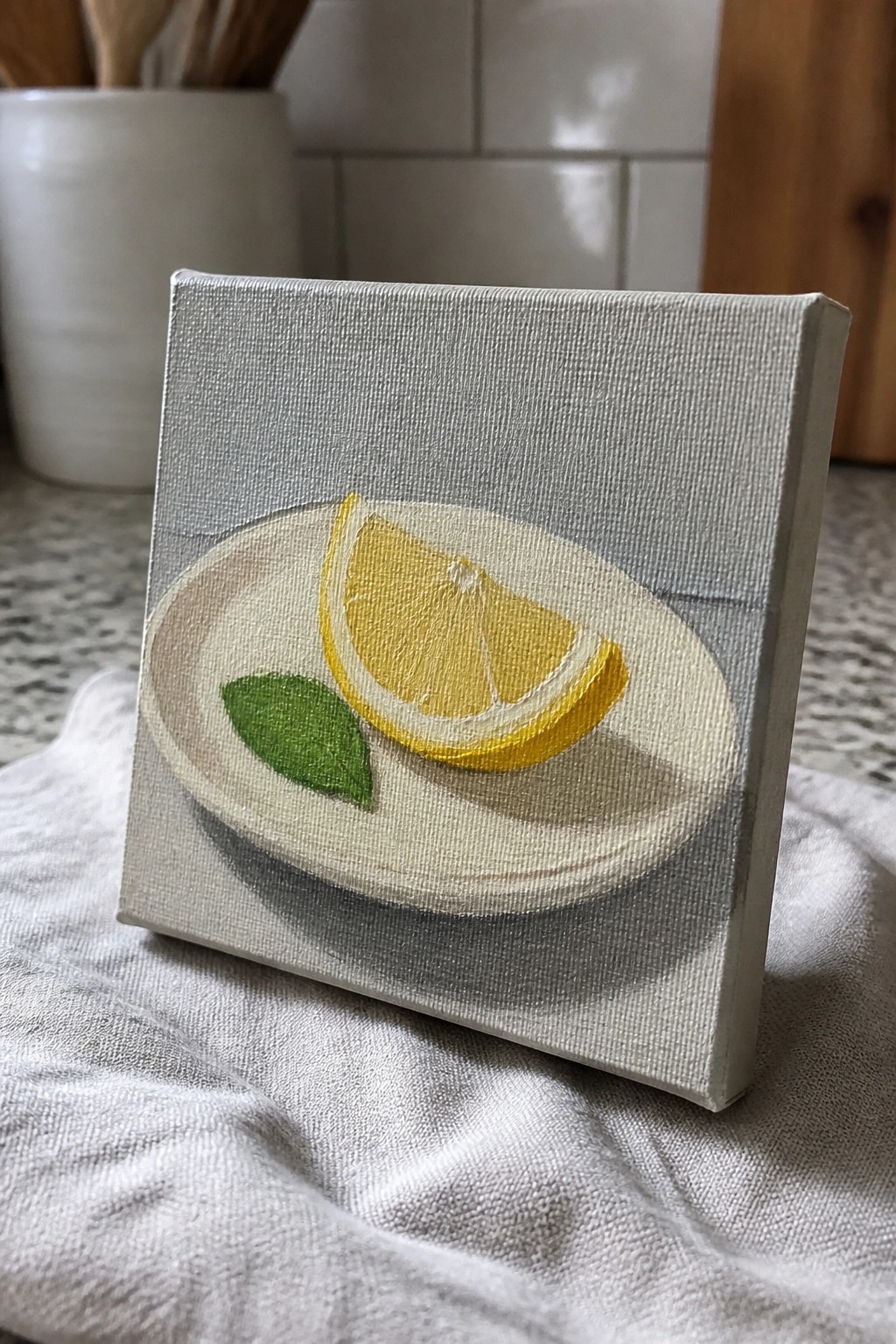 Small canvas painting of lemon wedge and green leaf on white plate