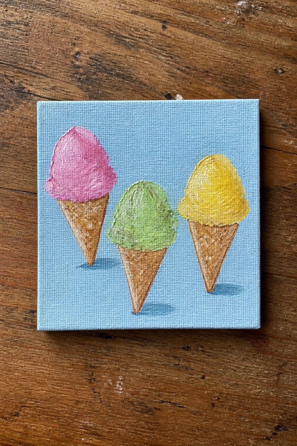 Three ice cream cones with pink, green, and yellow scoops on blue canvas.